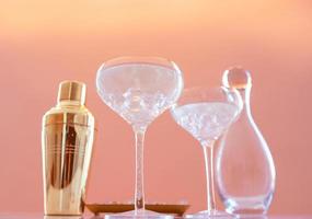 golden shaker, glass decanter, elegant glasses with cocktail and ice on beige background. Alcohol, party, hotel, bar concept photo