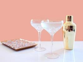 golden shaker, glass decanter, elegant glasses with cocktail and ice on beige background. Alcohol, party, hotel, bar concept photo