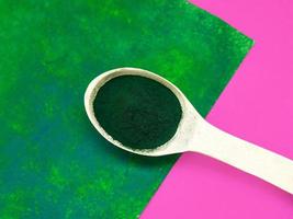 Green hawaiian spirulina in powder in wooden spoon on pink background. Super food, healthy lifestyle, healthy supplements concept photo