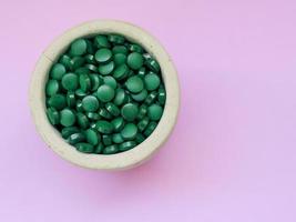 Green hawaiian spirulina in tablespoons pills on light lilac background. Super food, healthy lifestyle, healthy supplements concept photo