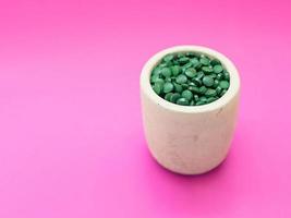Green hawaiian spirulina in tablespoons pills on light lilac background. Super food, healthy lifestyle, healthy supplements concept photo