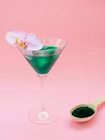 Liquid spirulina green drink in cocktail glass and spirulina pills on pink background. Super food, healthy lifestyle, healthy supplements concept photo