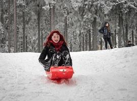una chica con trineos de pelo rojo en la nieve del invierno en el bosque. foto