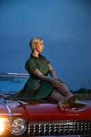 A beautiful girl poses on the hood of a red convertible Caddy, evening, sunset. photo