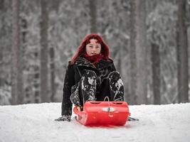 A girl with red hair sleds on the winter snow in the forest. photo