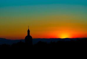 la impresionante belleza y los colores de la puesta de sol con vistas a las siluetas de los alpes y la silueta de una hermosa iglesia foto