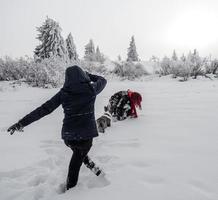 Two girls, sisters, play with a corgi dog on a snowy field in the mountains photo