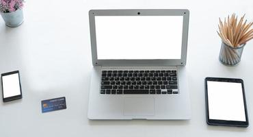 computadora portátil o portátil, tableta y teléfono inteligente, pantalla blanca en blanco, colocada en el escritorio junto a la ventana en casa u oficina. foto