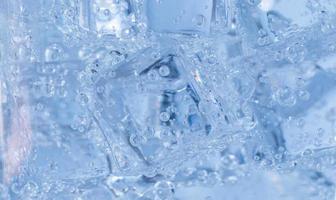 los cubitos de hielo con burbujas de aire se arremolinan en el vaso. agua de soda y enfriar en un vaso transparente. foto