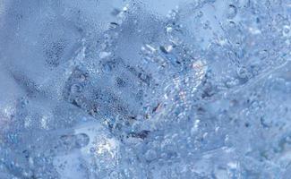 los cubitos de hielo con burbujas de aire se arremolinan en el vaso. agua de soda y enfriar en un vaso transparente.