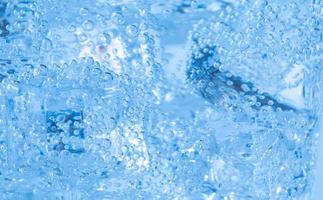 los cubitos de hielo con burbujas de aire se arremolinan en el vaso. agua de soda y enfriar en un vaso transparente. foto