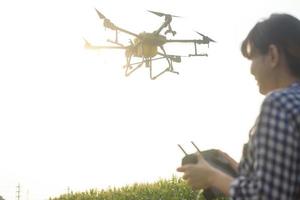 Young smart farmer controlling drone spraying fertilizer and pesticide over farmland,High technology innovations and smart farming photo