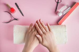 procedimiento de spa para el cuidado de las uñas en un salón de belleza. manos femeninas y herramientas para manicura sobre fondo rosa. foto