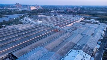 Roofs of Factory buildings in heavy industrial with white smoke against blue sky during sunset. Aerial photo view by drone from top of plant.