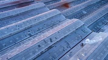 Roofs of Factory buildings in heavy industrial with white smoke against blue sky during sunset. Aerial photo view by drone from top of plant.