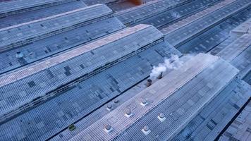 Roofs of Factory buildings in heavy industrial with white smoke against blue sky during sunset. Aerial photo view by drone from top of plant.