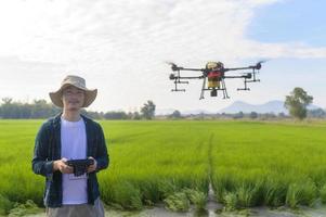 Young smart farmer controlling drone spraying fertilizer and pesticide over farmland,High technology innovations and smart farming photo