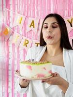 hermosa mujer celebrando la fiesta de cumpleaños sosteniendo un pastel, soplando velas foto