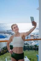 Happy woman in swimsuit taking selfie standing on the balcony of the hotel room photo