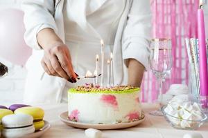 Woman in white party clothes preparing birthday table, lighting the candles photo