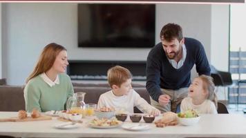 jeune famille heureuse parlant tout en prenant son petit déjeuner à la table à manger de l'appartement video