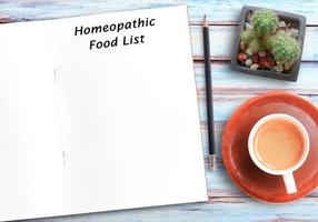 texto de la lista de alimentos homeopáticos en un cuaderno en blanco, lápiz y café en el fondo de la mesa de madera foto