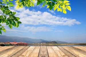 Green leaves and wooden table with blured blue sky background photo