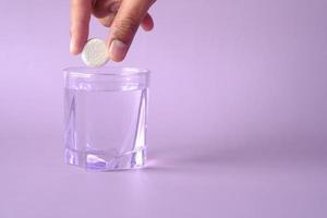 Effervescent soluble tablet pills and glass of water on purple background