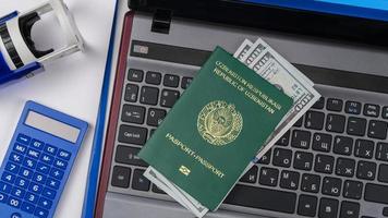 pasaporte de uzbekistán con dólares estadounidenses en el teclado de la computadora portátil. Registro en línea. concepto - soborno y corrupción. vista superior foto