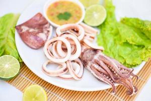 Squid rings on white plate, Fresh squid cooked boiled with lettuce vegetable salad lemon lime and seafood sauce on table background photo