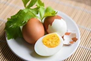 desayuno de huevos, menú de huevos frescos pelados, comida, huevos cocidos y cáscara de huevo en un plato blanco decorado con hojas de apio verde sobre fondo de madera, concepto de alimentación saludable para cocinar huevos foto