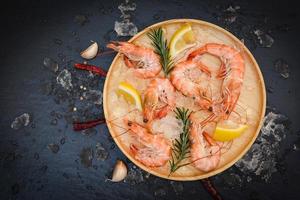fresh shrimps on ice with herbs and spices lemon chili garlic rosemary on wooden plate, boiled shrimp prawns cooked in the seafood restaurant photo