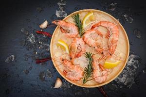 camarones frescos en hielo con hierbas y especias limón chile ajo romero en plato de madera, camarones hervidos cocinados en el restaurante de mariscos foto