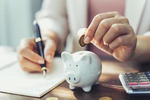 Closeup of business woman hand putting money coin into piggy bank for saving money. saving money and financial concept photo