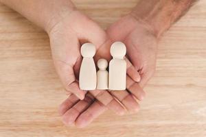 Man husband and Woman wife hands holding wooden peg dolls on the wood table background. family home, foster care, homeless charity support concept, family mental health. photo