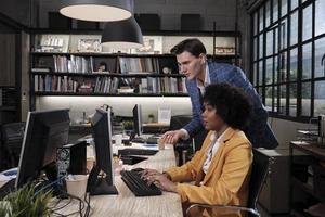 Young African American female worker sits, works with computer, brainstorming, talking, and discussing with Caucasian male colleague and partnership about business jobs in workspace office company. photo