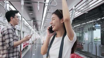 dois jovens passageiros em pé no trem do céu vazio, linda mulher asiática com turista de câmera falando em um telefone celular, viajar com transporte ferroviário urbano da tailândia, férias de viagem de estilo de vida feliz. video