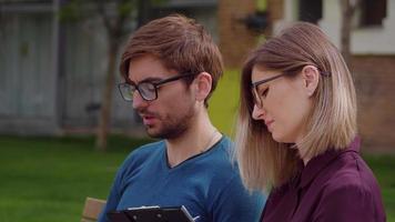 Two professional coworkers discuss, Close up portrait sitting on bench spring background. video