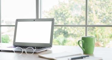 Laptop or notebook computer, blank white screen, placed on the desk by the window at home or office. photo