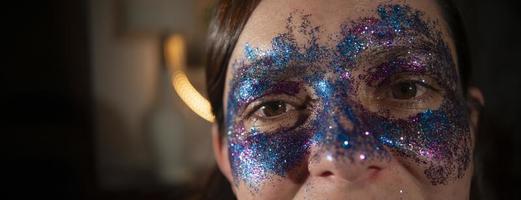 Close up of a beautiful woman's eyes made up with blue and purple particles forming a mask against a dark out of focus background photo