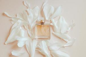 Perfume bottle and flower petals on pastel beige background. Natural cosmetics with aromatic oil.