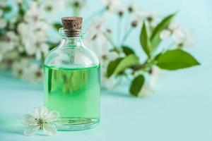 Aromatic essential oil in glass bottle and flowers on blue background. Aromatherapy and spa concept.