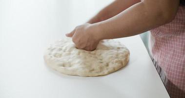Women knead the dough by hand to avoid air bubbles on a white table, 4K video