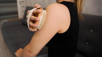 Young woman uses a dry brush to self-massage her arms and shoulders photo