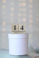 Valentine's day concept. Date 14 February on wooden cube calendar on a white gift box and white heart in hand. Bokeh golden and white background photo