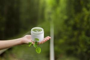 Young Female hand hold a jar of green natural cream for face or body. organic natural skincare products on green natural background. Packaging of lotion or cream. Beauty cosmetic skin care concept. photo