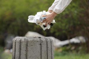 la mujer tira basura plástica a la basura. mano de mujer recogiendo plástico de basura para limpiar en el parque. recolección de basura después de una pandemia. enfoque selectivo foto