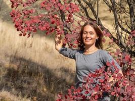 mujer sonriente cerca de un árbol con hojas rojas, retrato de otoño foto