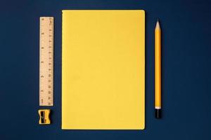 top view pastel yellow notebook with yellow pencil and notepad on navy blue working table photo