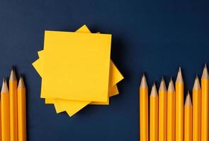 blank yellow sticky note and pencil on navy blue table background photo